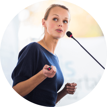 Lady speaker at an event talking into microphone with a pen pointer in hand to control the information screen displayed to the audience. Experience and understanding from a Specialist Events Production team who combine Virtual and Live Events: CODA Communications